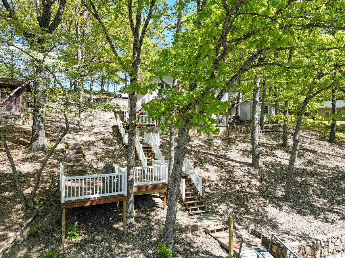 A view from the lower hillside with a staircase leading up through lush greenery to spacious elevated decks. The decks overlook the natural surroundings and offer inviting spaces for outdoor gatherings and enjoying sunrises or starlit evenings.