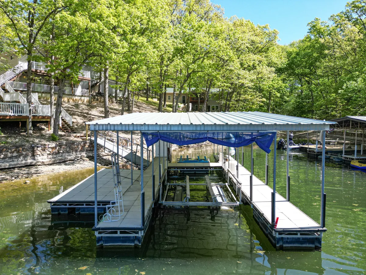 This image captures the boat dock at the water's edge, surrounded by lush trees and the tranquil surface of the lake. People can be seen fishing, preparing a boat, or simply relaxing by the water, with hints of sunset reflecting on the dock.