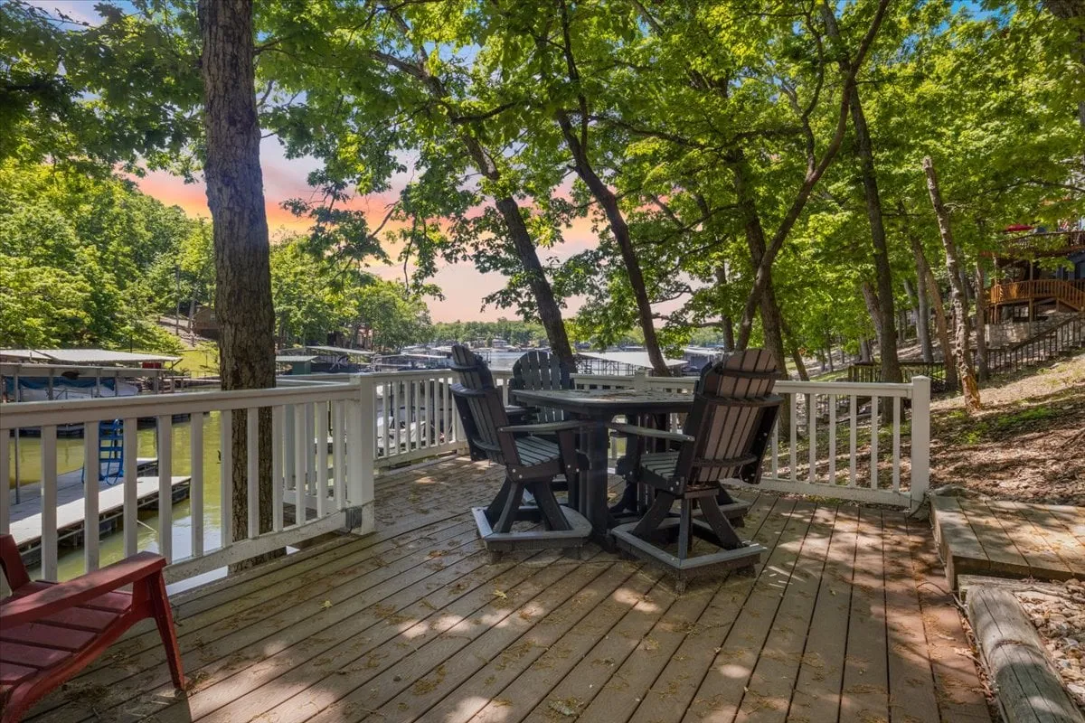 A spacious wooden deck furnished with an outdoor dining set overlooks the tranquil lake. Surrounded by trees, the deck offers a peaceful atmosphere with stunning water views, ideal for social gatherings or quiet relaxation outdoors.