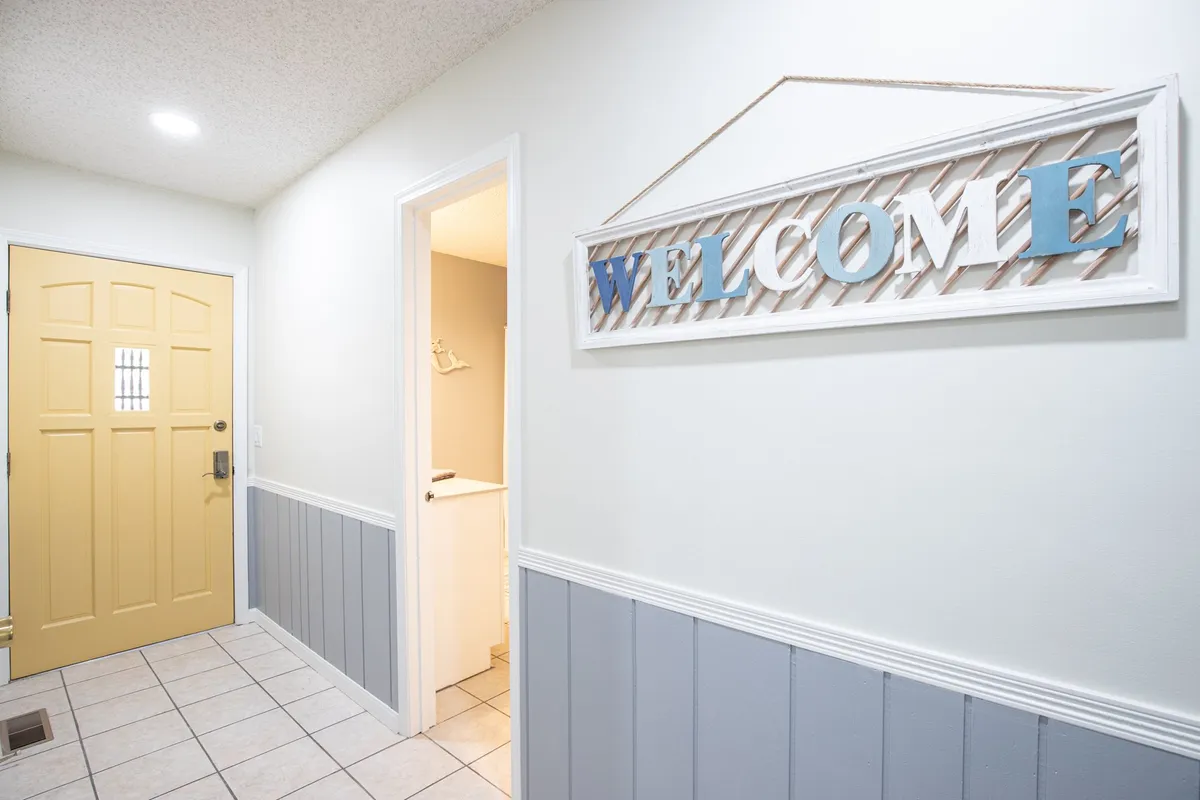 This image showcases the welcoming yellow front door with a 'WELCOME' sign and a textured wall, setting a positive first impression for arriving guests. The door is bright and inviting, suggesting a sense of arrival and anticipation for the stay.