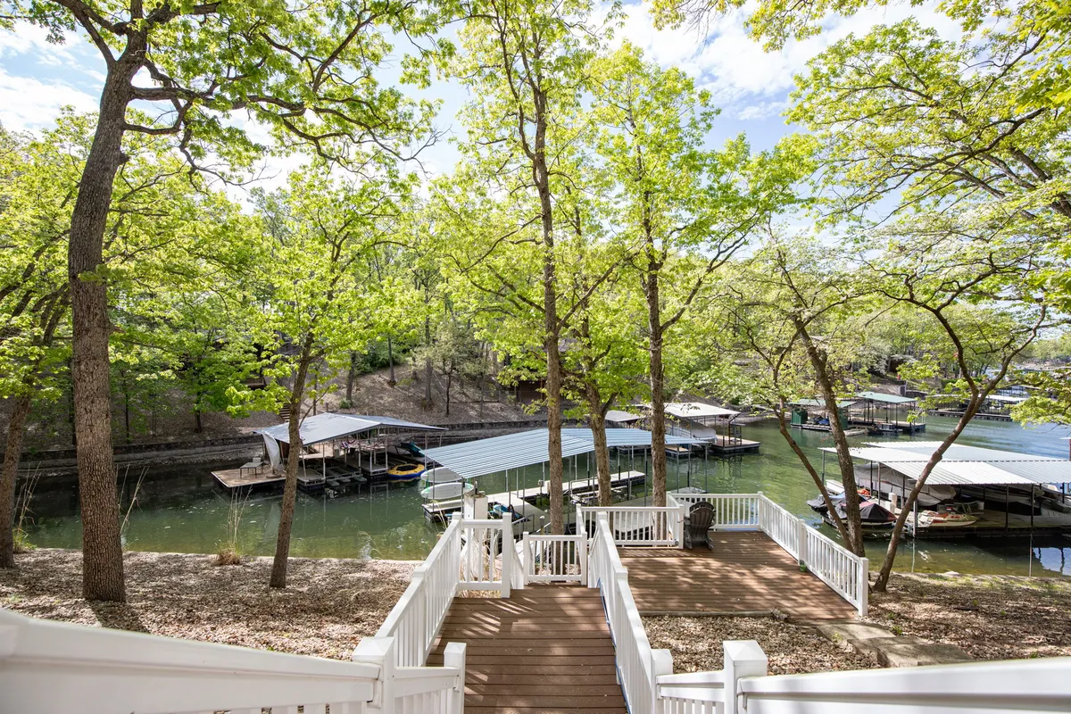 A wide view of the property’s wooden stairs leading down to the waterfront, framed by green trees and neighboring boathouses. The scene is peaceful, with calm water inviting boating, fishing, and easy access for all ages.
