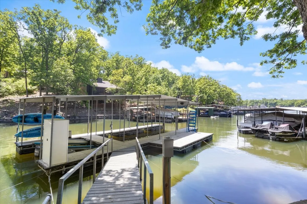 This image captures a serene lakeside dock surrounded by trees, with boats moored in the calm water. The setting sun reflects off the water, highlighting the tranquil atmosphere and inviting opportunities for boating, fishing, or simply relaxing by the shore.