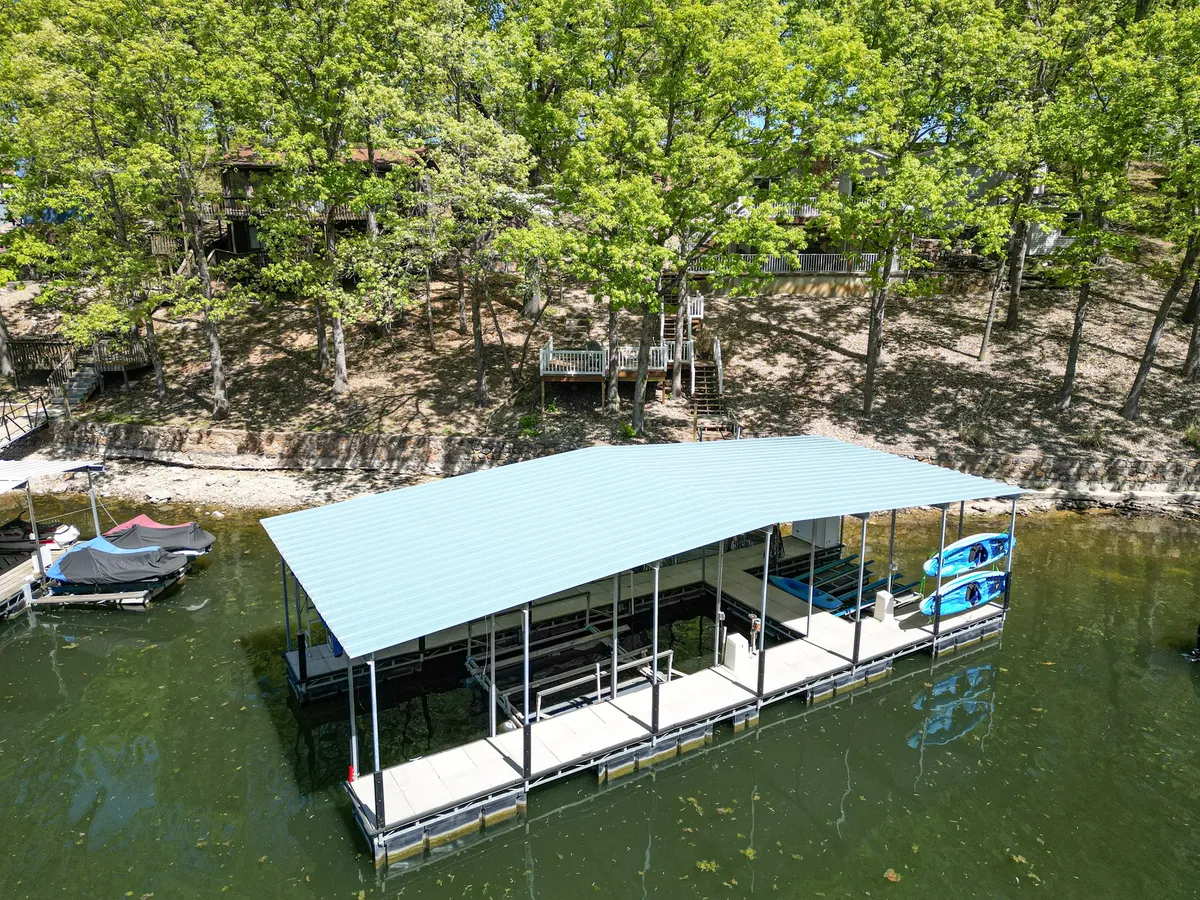 A private dock extends over the water with kayaks ready for launch. The scene is framed by lush trees, and the calm water invites guests to enjoy boating, fishing, or simply relaxing by the shore.
