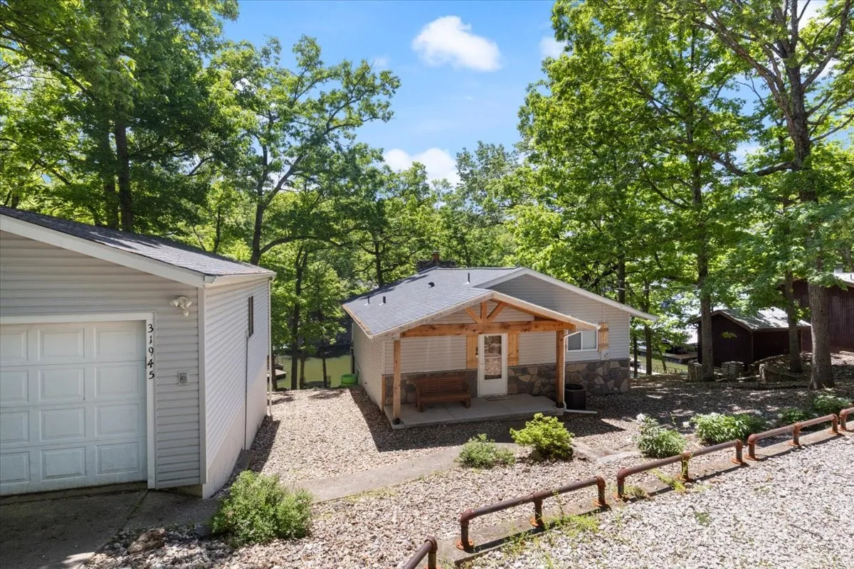 An inviting exterior view of the house, featuring the porch, garage, and lush greenery. The porch offers a comfortable spot to relax and enjoy the tranquil surroundings, highlighting the welcoming atmosphere.