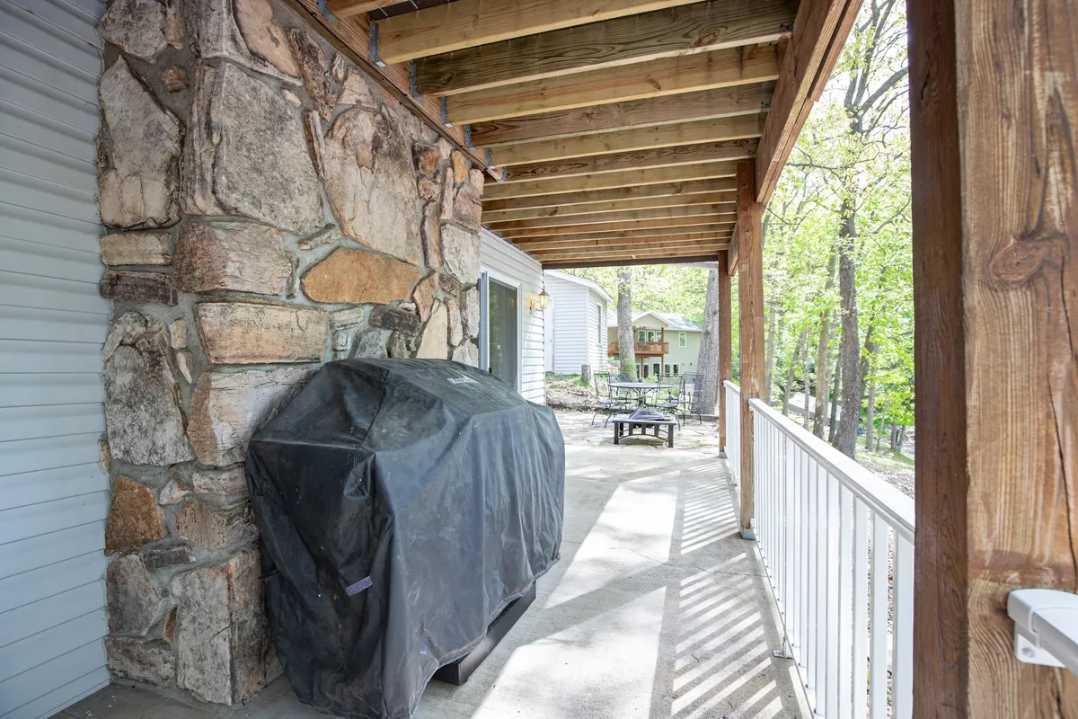 An exterior shot of a stone-walled patio with a grill, covered seating, and wooden beams, set against a lush backdrop. The area is ready for outdoor dining and lakeside barbecues, inviting guests to gather and relax after a day on the water.