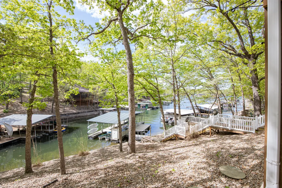 A serene view of a wooden deck overlooking calm water, with boats moored at docks and lush green trees surrounding the area. The setting is ideal for group gatherings, boating activities, and taking in the beauty of the lake at sunset or during the day.