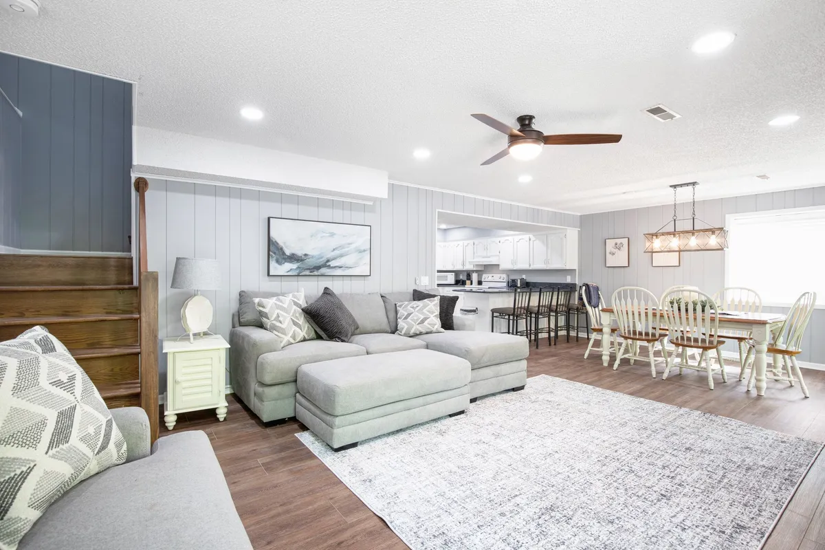 An open-concept living space with a cozy sectional sofa, a spacious dining table, and a glimpse into the kitchen, all framed by tasteful décor and soft lighting. The environment exudes warmth and sociability, perfect for family gatherings or relaxing after a day of lakeside adventures.