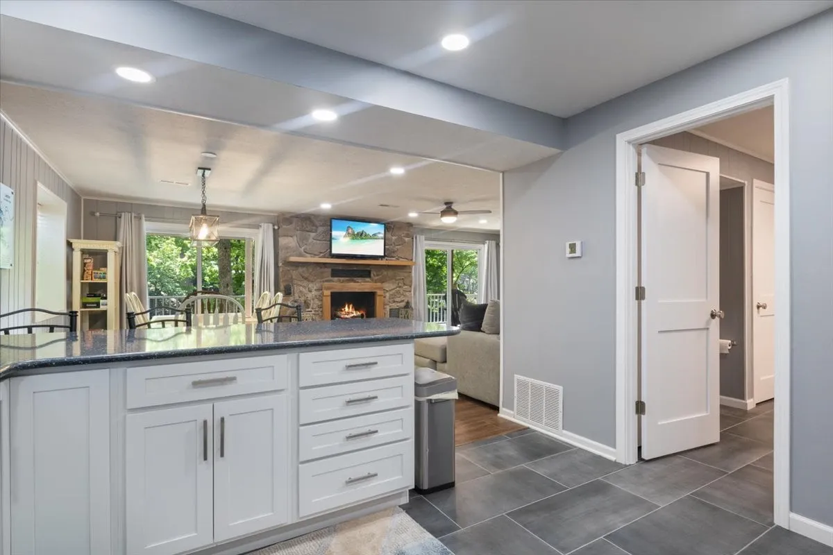 A spacious, light-filled kitchen and dining area with a central island, fireplace, and windows offering green views. The area invites cooking, entertaining, and enjoying meals together, with visual access to the surrounding natural beauty.