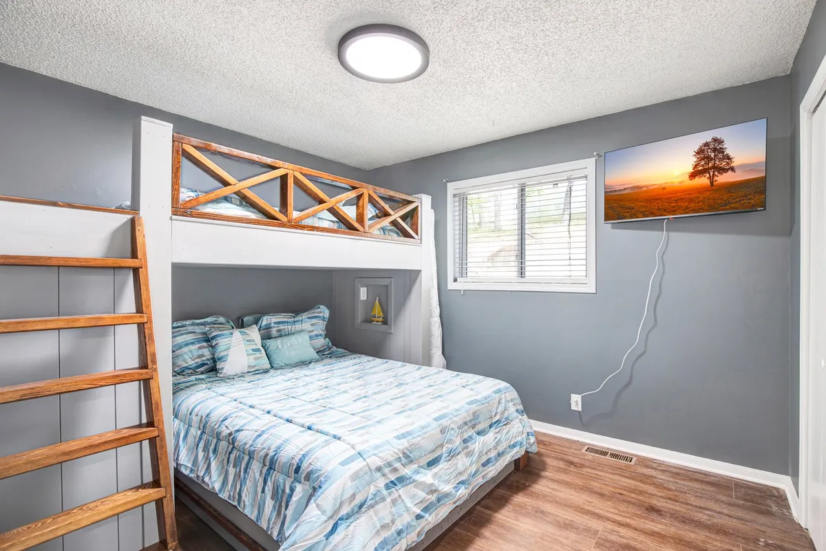 A relaxed bedroom scene with a bunk bed, decorative pillows, and a wall-mounted TV. The space is designed for both comfort and fun, ideal for kids or groups enjoying movie nights or sleepovers. The arrangement suggests flexible sleeping options for families or larger groups.